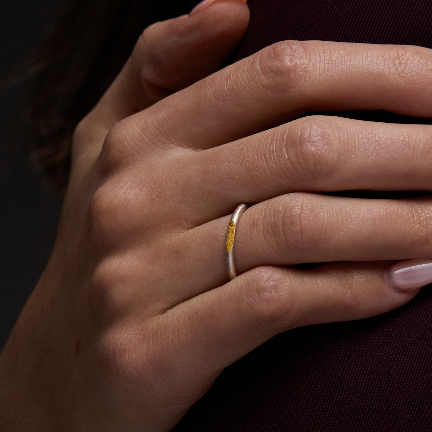 Close-up of a hand with a silver and gold ring on a dark background