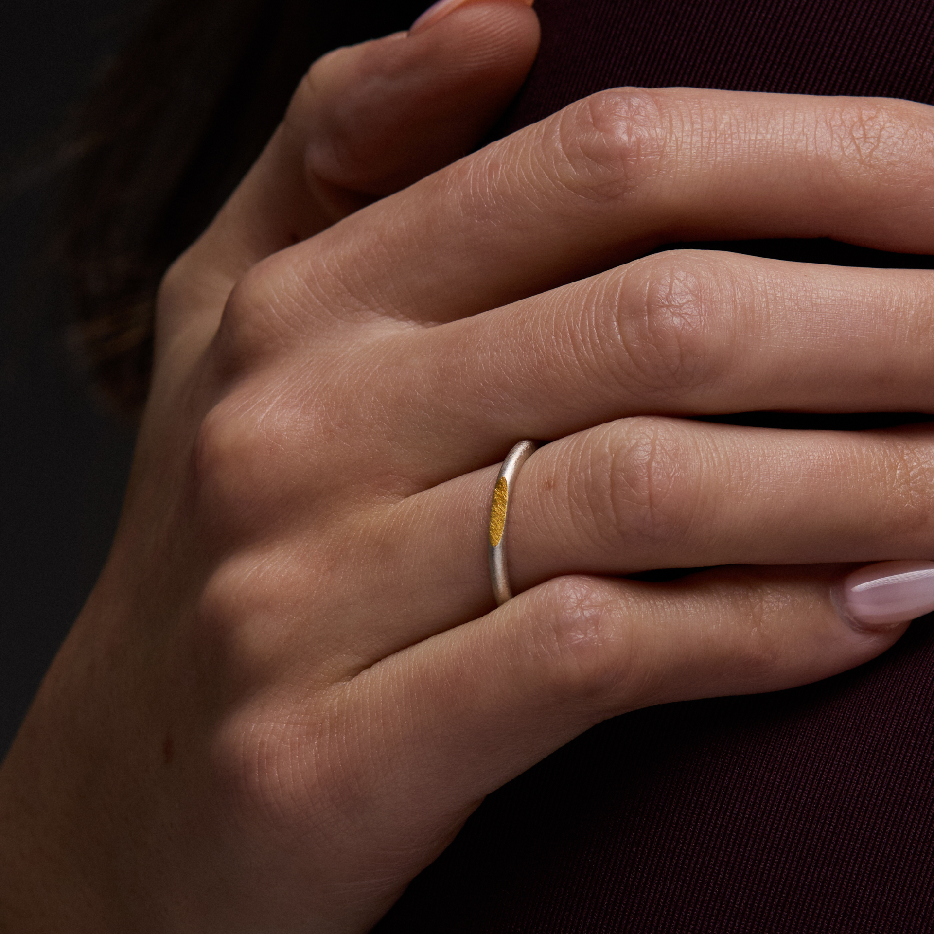 Close-up of a hand with a silver and gold ring on a dark background