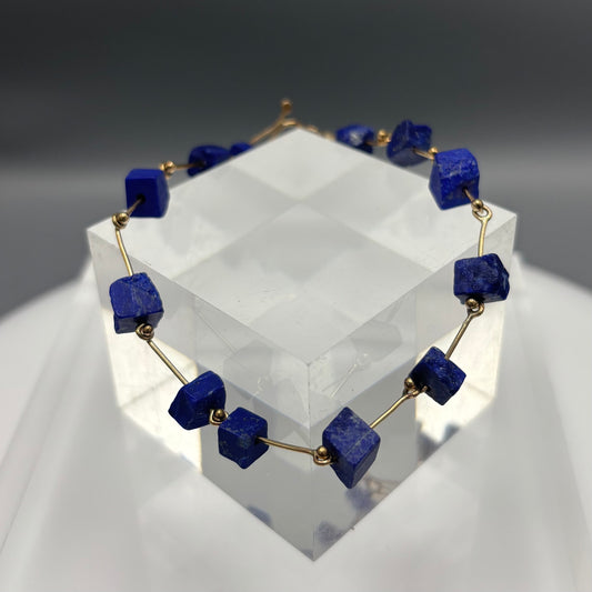 Necklace with blue square beads on a clear stand against a gray background