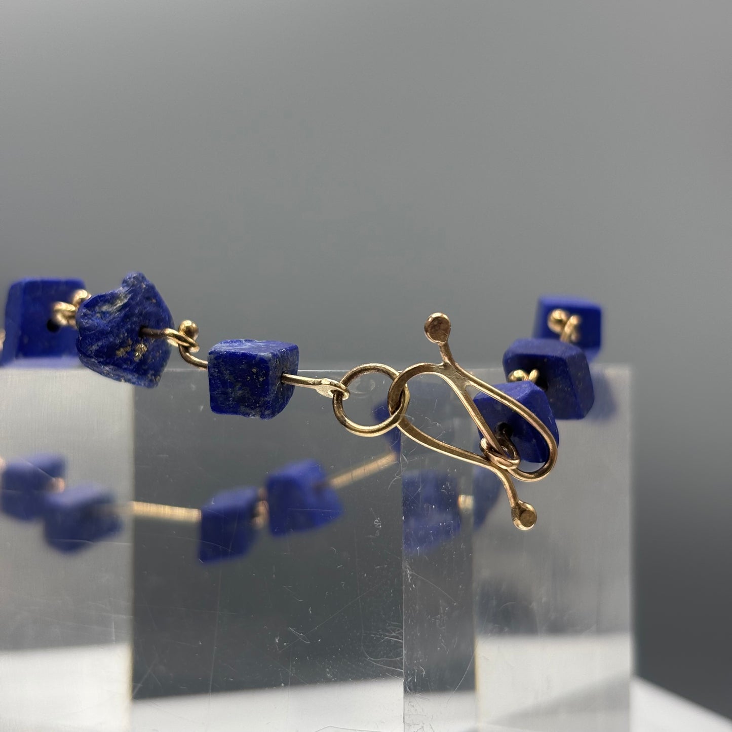 Bracelet with blue beads and gold accents on a clear stand against a gray background