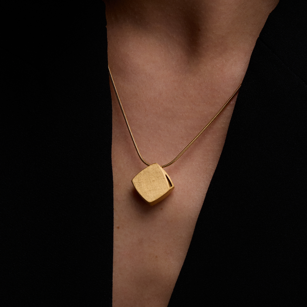 Gold necklace with a square pendant on a dark background